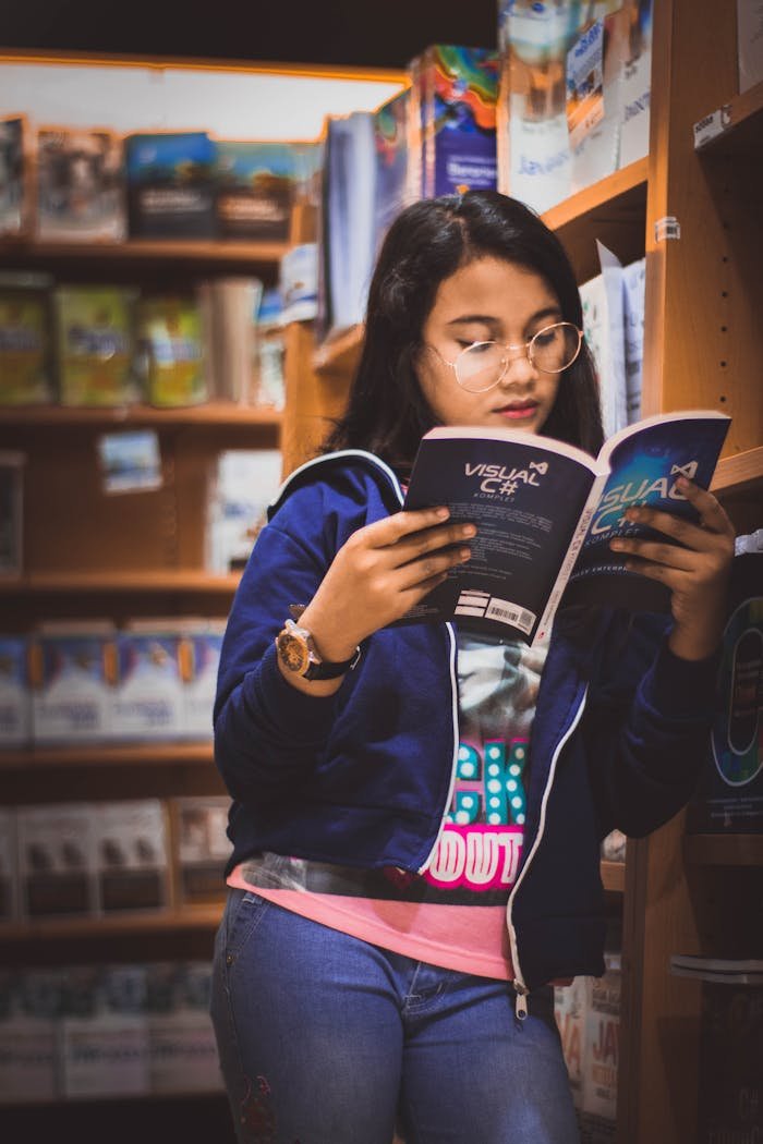 A young woman engrossed in a book inside a cozy and well-lit bookstore, surrounded by shelves.